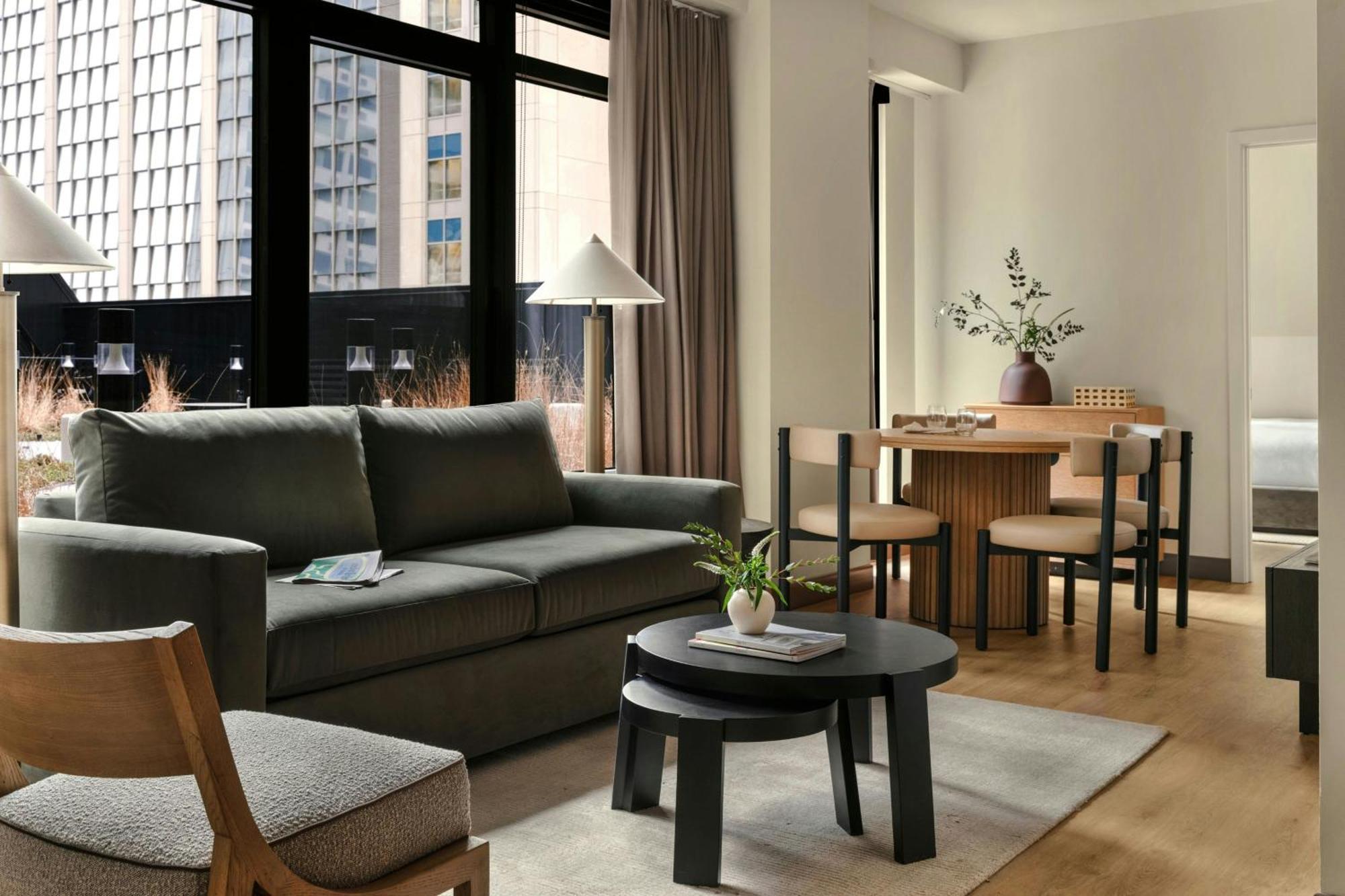 Sonder suite living area with an olive sofa, oak dining table, and city views